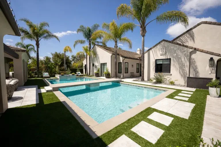 Backyard artificial turf lawn bordered by deck steps and a perimeter wall.